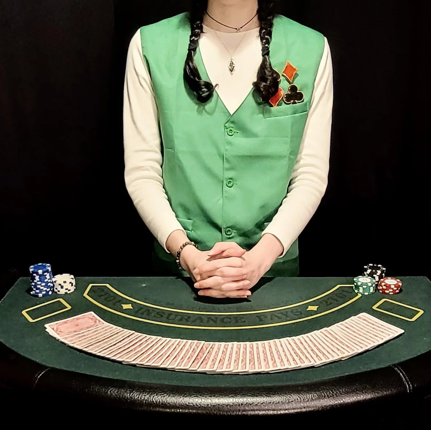 Casino dealer in a green vest standing behind a card table in the Royale Casino Heist escape room
